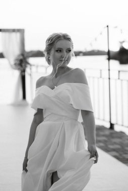 Gelin, sarı bir günbatımının arka planında nehir kıyısındaki bir iskelede