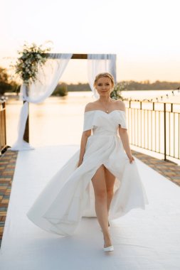 Gelin, sarı bir günbatımının arka planında nehir kıyısındaki bir iskelede