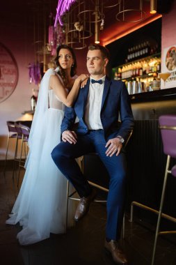 Gelin ve damat bir kokteyl barının içinde. Parlak bir atmosferde, bir bardak içkiyle.