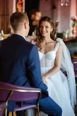 Gelin ve damat bir kokteyl barının içinde. Parlak bir atmosferde, bir bardak içkiyle.