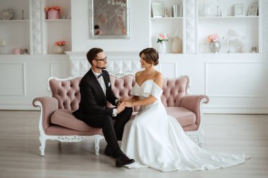 Siyah takım elbiseli damat papyonlu ve parlak bir stüdyoda dar beyaz elbiseli gelin.