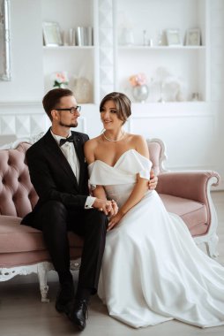 Siyah takım elbiseli damat papyonlu ve parlak bir stüdyoda dar beyaz elbiseli gelin.