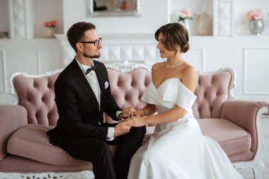 Siyah takım elbiseli damat papyonlu ve parlak bir stüdyoda dar beyaz elbiseli gelin.