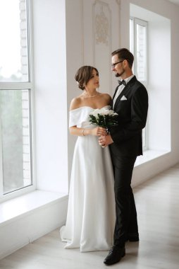 Siyah takım elbiseli damat papyonlu ve parlak bir stüdyoda dar beyaz elbiseli gelin.