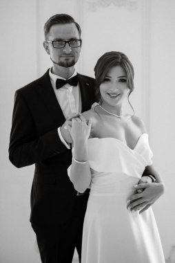 Siyah takım elbiseli damat papyonlu ve parlak bir stüdyoda dar beyaz elbiseli gelin.