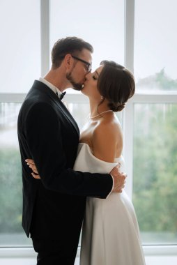 Siyah takım elbiseli damat papyonlu ve parlak bir stüdyoda dar beyaz elbiseli gelin.
