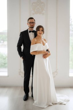 Siyah takım elbiseli damat papyonlu ve parlak bir stüdyoda dar beyaz elbiseli gelin.