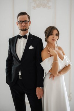 Siyah takım elbiseli damat papyonlu ve parlak bir stüdyoda dar beyaz elbiseli gelin.