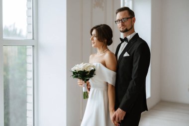 Siyah takım elbiseli damat papyonlu ve parlak bir stüdyoda dar beyaz elbiseli gelin.