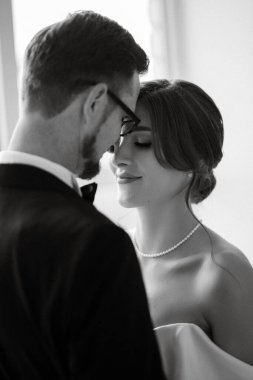 Siyah takım elbiseli damat papyonlu ve parlak bir stüdyoda dar beyaz elbiseli gelin.