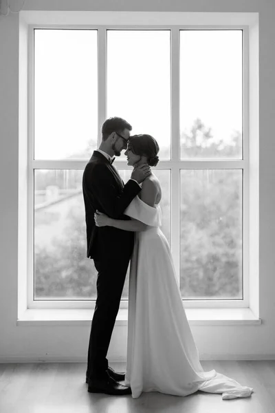 ブウタイと花嫁と黒のスーツの新郎明るいスタジオでタイトな白いドレス — ストック写真