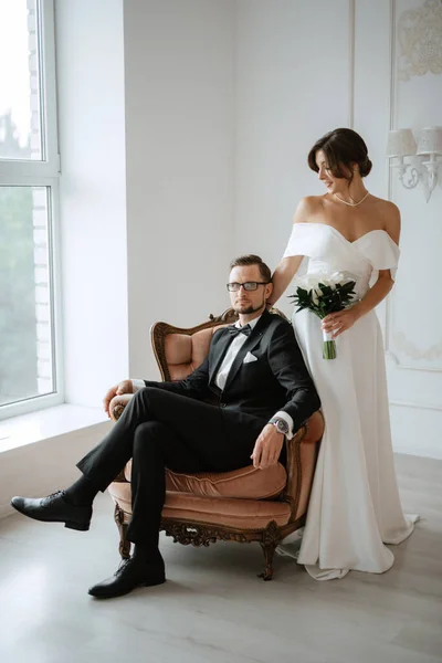 ブウタイと花嫁と黒のスーツの新郎明るいスタジオでタイトな白いドレス — ストック写真