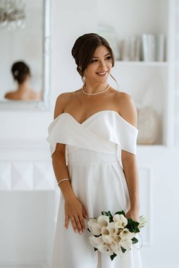 Parlak bir stüdyoda, dar bir gelinlik içinde, buketi olan esmer gelin.
