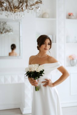 Parlak bir stüdyoda, dar bir gelinlik içinde, buketi olan esmer gelin.