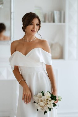 Parlak bir stüdyoda, dar bir gelinlik içinde, buketi olan esmer gelin.