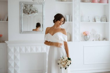 Parlak bir stüdyoda, dar bir gelinlik içinde, buketi olan esmer gelin.