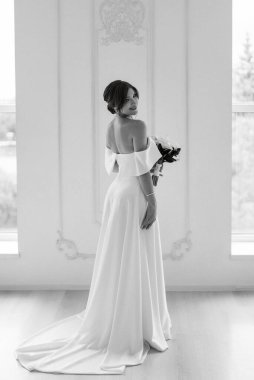 Parlak bir stüdyoda, dar bir gelinlik içinde, buketi olan esmer gelin.