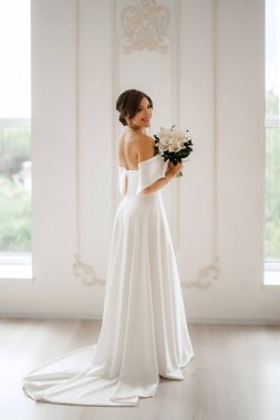 Parlak bir stüdyoda, dar bir gelinlik içinde, buketi olan esmer gelin.