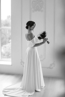 Parlak bir stüdyoda, dar bir gelinlik içinde, buketi olan esmer gelin.