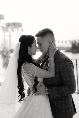 Gelin ve damat, nehrin kıyısındaki bir iskelede sarı bir günbatımının arkaplanına karşı.