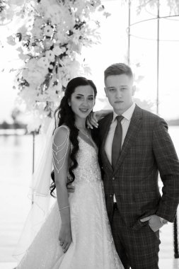 Gelin ve damat, nehrin kıyısındaki bir iskelede sarı bir günbatımının arkaplanına karşı.