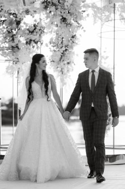 Gelin ve damat, nehrin kıyısındaki bir iskelede sarı bir günbatımının arkaplanına karşı.