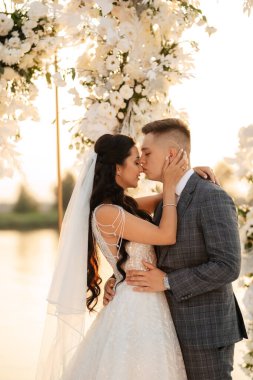 Gelin ve damat, nehrin kıyısındaki bir iskelede sarı bir günbatımının arkaplanına karşı.