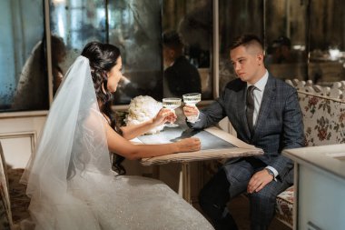 Gelin ve damat bir kokteyl barının içinde. Parlak bir atmosferde, bir bardak içkiyle.