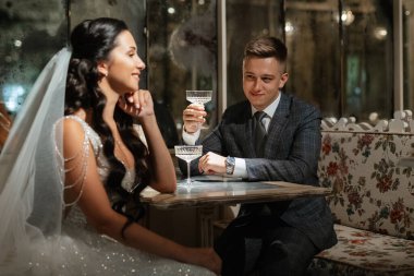 Gelin ve damat bir kokteyl barının içinde. Parlak bir atmosferde, bir bardak içkiyle.