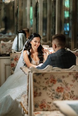 Gelin ve damat bir kokteyl barının içinde. Parlak bir atmosferde, bir bardak içkiyle.