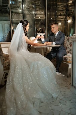 Gelin ve damat bir kokteyl barının içinde. Parlak bir atmosferde, bir bardak içkiyle.