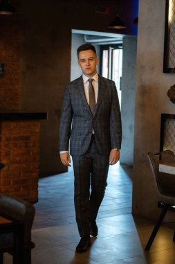 Gri ekose takım elbiseli bir damadın portresi. Düğün günü bir barda kravat takmış.