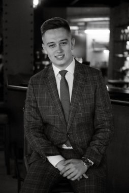 Gri ekose takım elbiseli bir damadın portresi. Düğün günü bir barda kravat takmış.