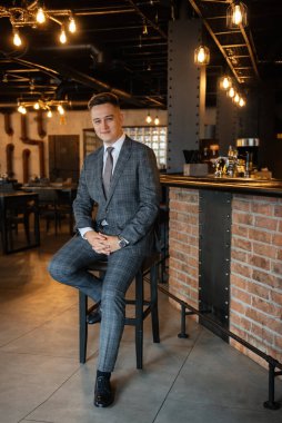 Gri ekose takım elbiseli bir damadın portresi. Düğün günü bir barda kravat takmış.