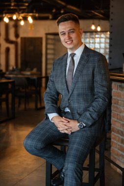 Gri ekose takım elbiseli bir damadın portresi. Düğün günü bir barda kravat takmış.