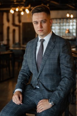 Gri ekose takım elbiseli bir damadın portresi. Düğün günü bir barda kravat takmış.