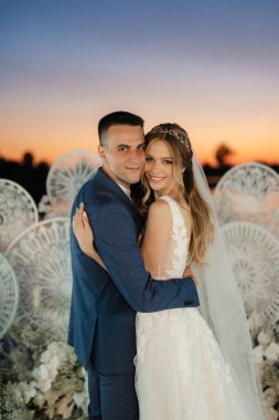 bride and groom against the backdrop of a yellow sunset on a pier near the river