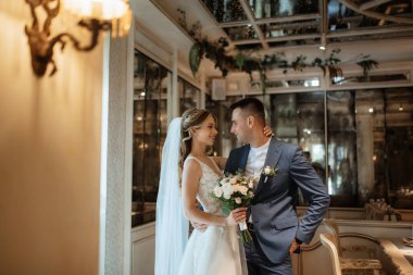 Gelin ve damat bir kokteyl barının içinde. Parlak bir atmosferde, bir bardak içkiyle.