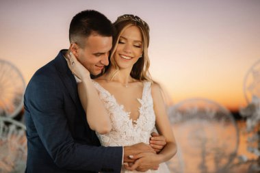 bride and groom against the backdrop of a yellow sunset on a pier near the river