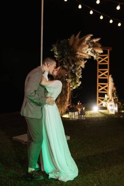 Gelin ve damadın ilk düğün dansı şehir kulübünün açıklarında gün batımı ve ılık çelenklerin ışığında.