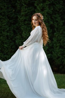 Yeşil thuja 'lı bir çayırda düğün buketi olan kızıl saçlı bir gelin.