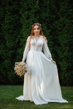 Yeşil thuja 'lı bir çayırda düğün buketi olan kızıl saçlı bir gelin.