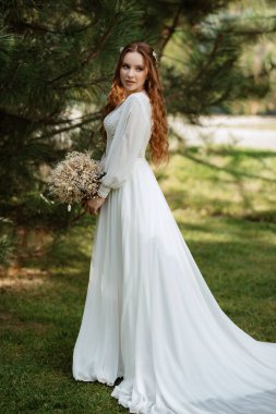 Yeşil thuja 'lı bir çayırda düğün buketi olan kızıl saçlı bir gelin.