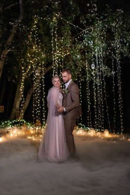 Gelin ve damadın ilk düğün dansı şehir kulübünün açıklarında gün batımı ve ılık çelenklerin ışığında.