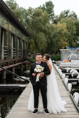 the first meeting of the bride and groom in wedding dresses on the pier near the water