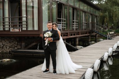 the first meeting of the bride and groom in wedding dresses on the pier near the water