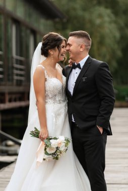 the first meeting of the bride and groom in wedding dresses on the pier near the water
