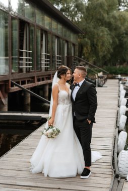 the first meeting of the bride and groom in wedding dresses on the pier near the water