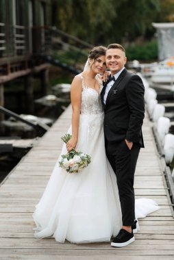 the first meeting of the bride and groom in wedding dresses on the pier near the water