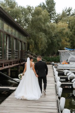 the first meeting of the bride and groom in wedding dresses on the pier near the water